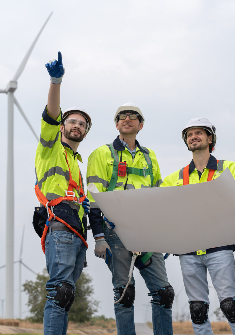 Team engineers in uniform with helmet safety pointing as they inspect a series of wind turbines