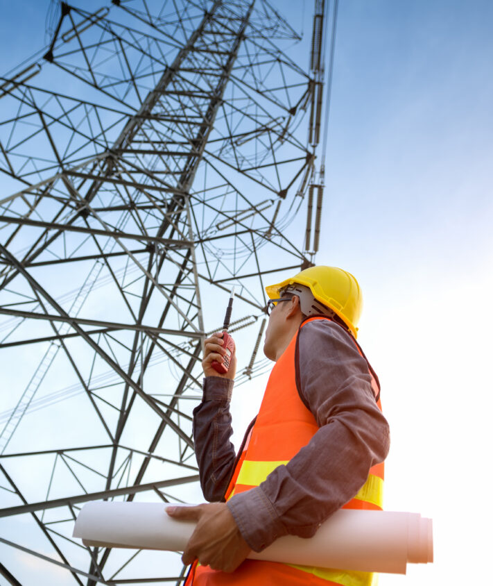 Electricity employee with hardhat staring up at a metal tower
