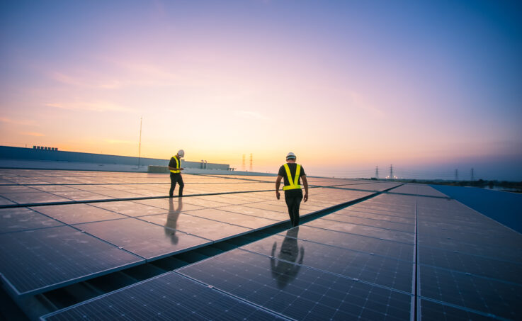 Des ingénieur·e·s inspectant des panneaux solaires installés sur un toit au coucher du soleil.