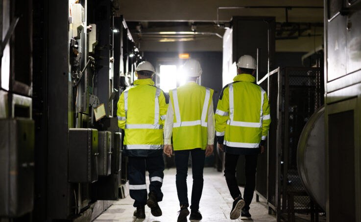 Three workers wearing safety gear walking together in a darkened facility