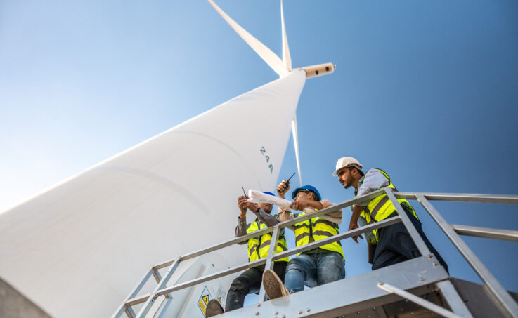 Engineers standing on a platform below a large white wind turbine