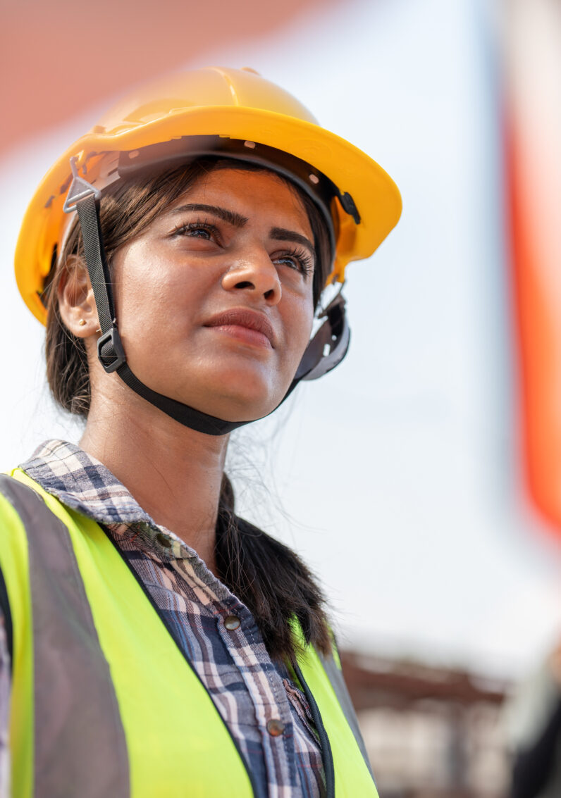 Confident female Indian engineer wearing protective helmet and vest on the job site